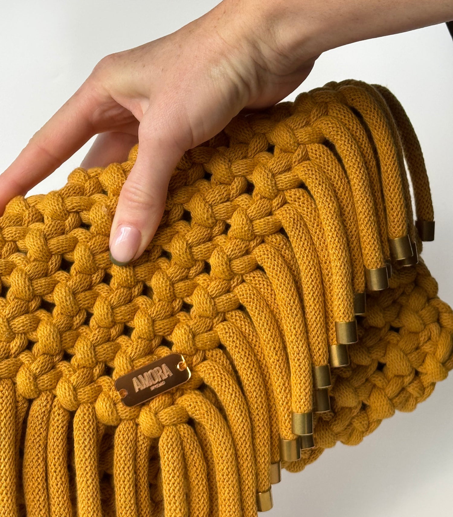 Hand holding a mustard yellow braided bag with gold accents on a white background