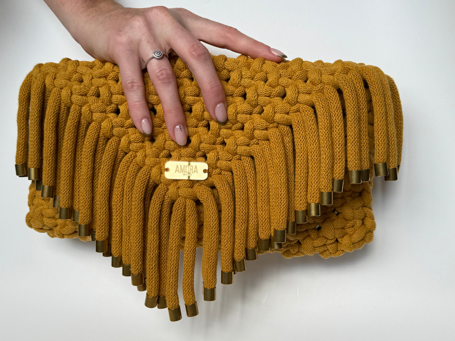 Mustard yellow woven clutch held by a hand on a white background