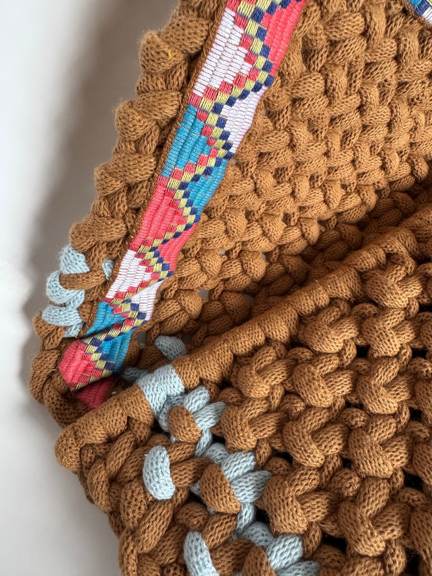 Close-up of a brown knitted blanket with colorful woven border on a white background